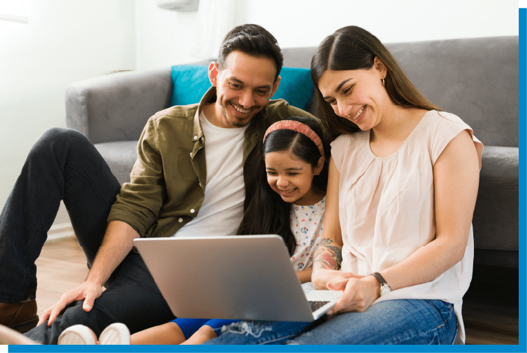 Family sitting together on the floor smiling while watching something on a laptop at home