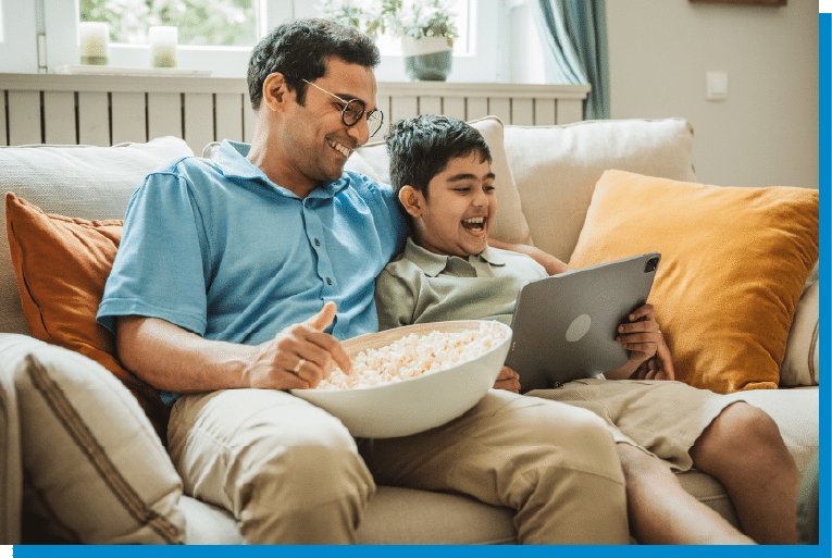 Father and son relaxing on the couch, sharing popcorn and watching a tablet together