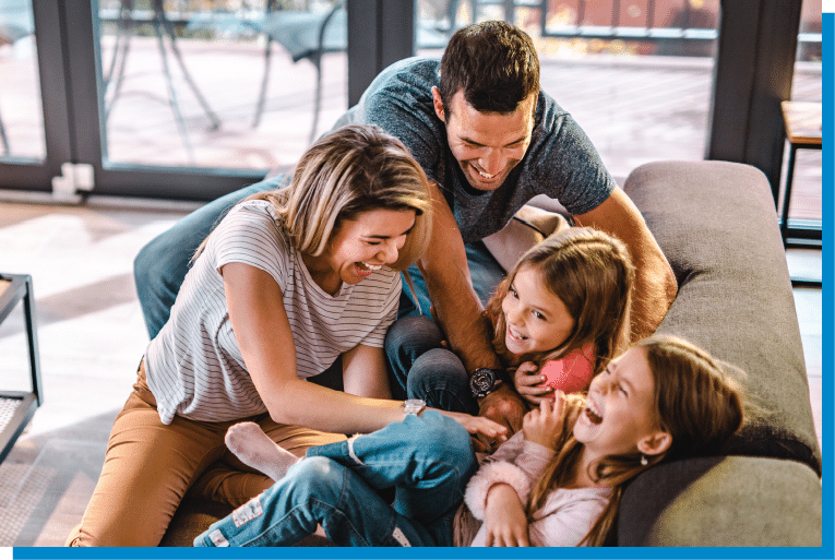 Parents laughing and playing with their two daughters on the living room couch during a fun family moment