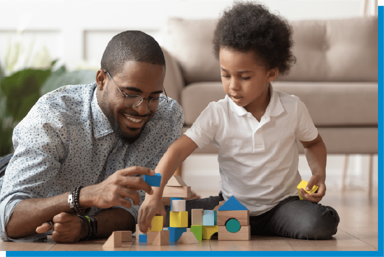 Father and young son playing with colorful wooden blocks on the living room floor