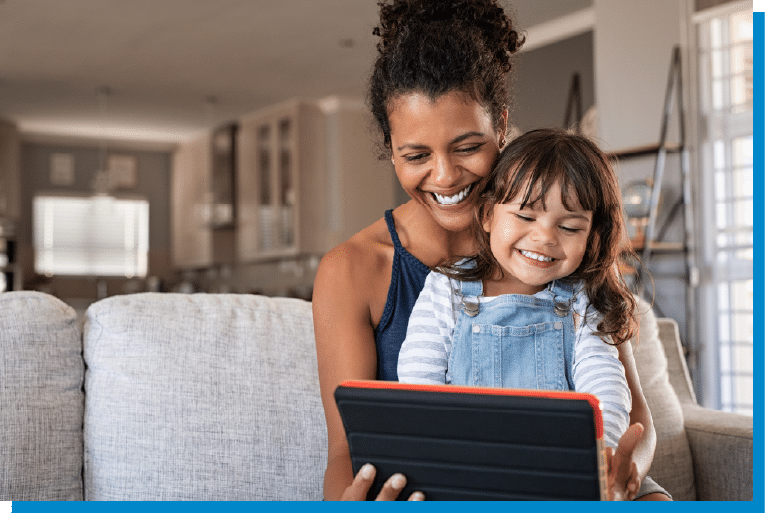 Mother and daughter smiling together while using a tablet at home